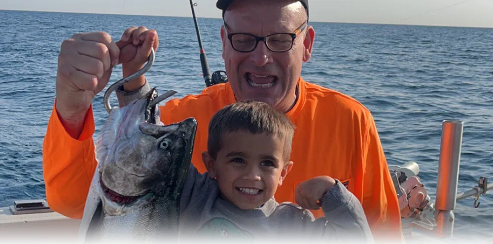 A man and a young boy pose with a salmon held up on a hook